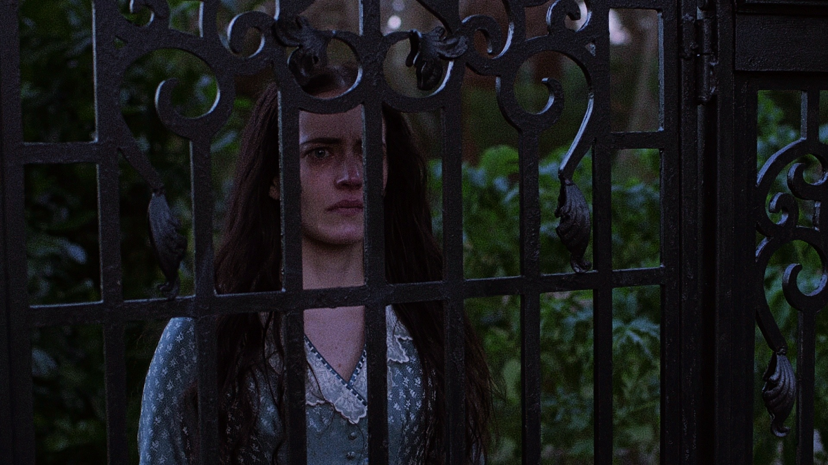 Vanessa standing behind an ornate wrought-iron gate, framed by serpentine ironwork and dim green foliage